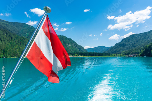Fototapeta Naklejka Na Ścianę i Meble -  Austria flag in the wind during a boat ride on a lake in the Alps.