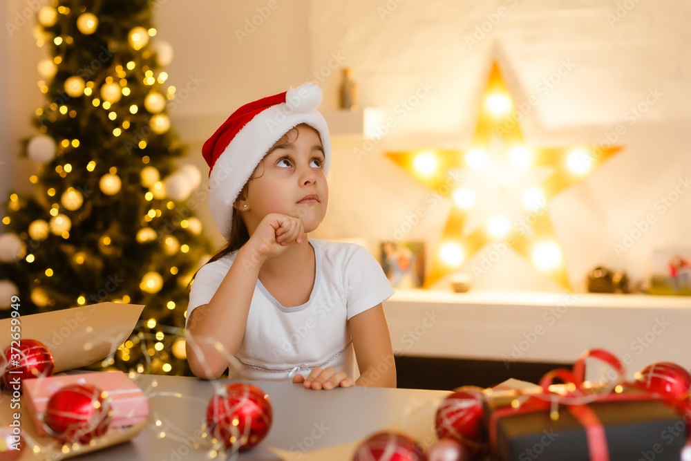 child girl in red hat preparing gifts for christmas at home, cozy holiday interior