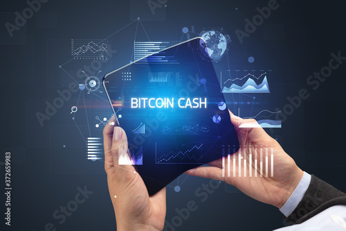 Businessman holding a foldable smartphone with BITCOIN CASH inscription, successful business concept