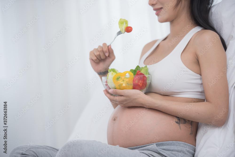 care about unborn child. pregnancy, healthy food and people concept, happy pregnant woman eating vegetable salad for breakfast sitting on bed at home. pregnancy and healthy organic nutrition. care about unborn child. pregnancy, healthy food and people concept, happy pregnant woman eating vegetable salad for breakfast sitting on bed at home. pregnancy and healthy organic nutrition.