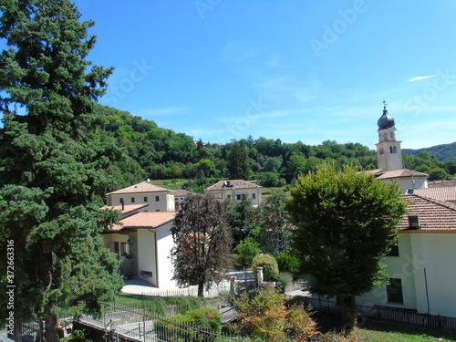 Tarzo, Italy - 08/15/2020: Beautiful photography of a little village from north Italy in summer days. View to the old church, mountains and some houses with grey and blue sky in background.