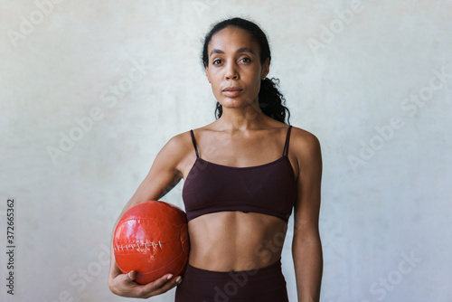 Photo of young african american sportswoman standing with medicine ball