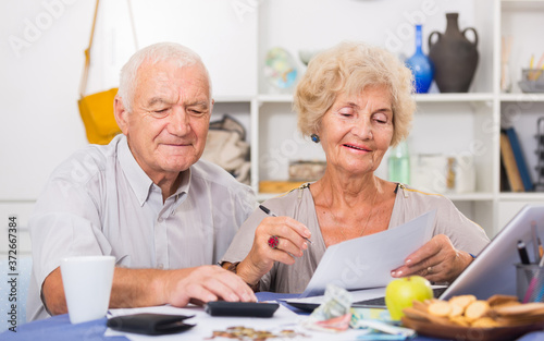 Portrait of happy senior spouses with bills and laptop while sitting at table at home