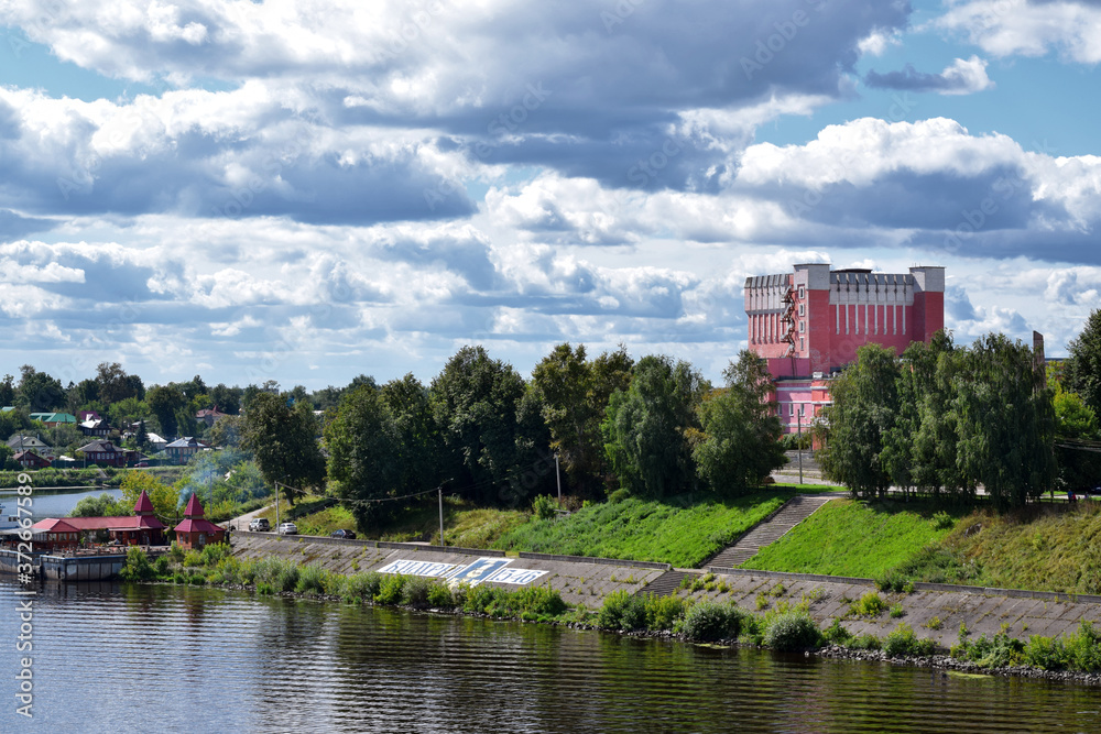 Fototapeta premium Kimry, Tver Region, Russia - August 19, 2020: View of the left bank of small town Kimry from the bridge. The building of the theater and the embankment on a sunny day
