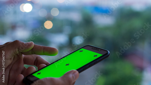 A man's hand holding a smartphone with a green screen is used for multimedia editing.