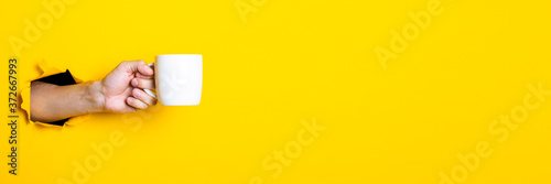Fotografie Man's hand holding a white cup on a bright yellow background