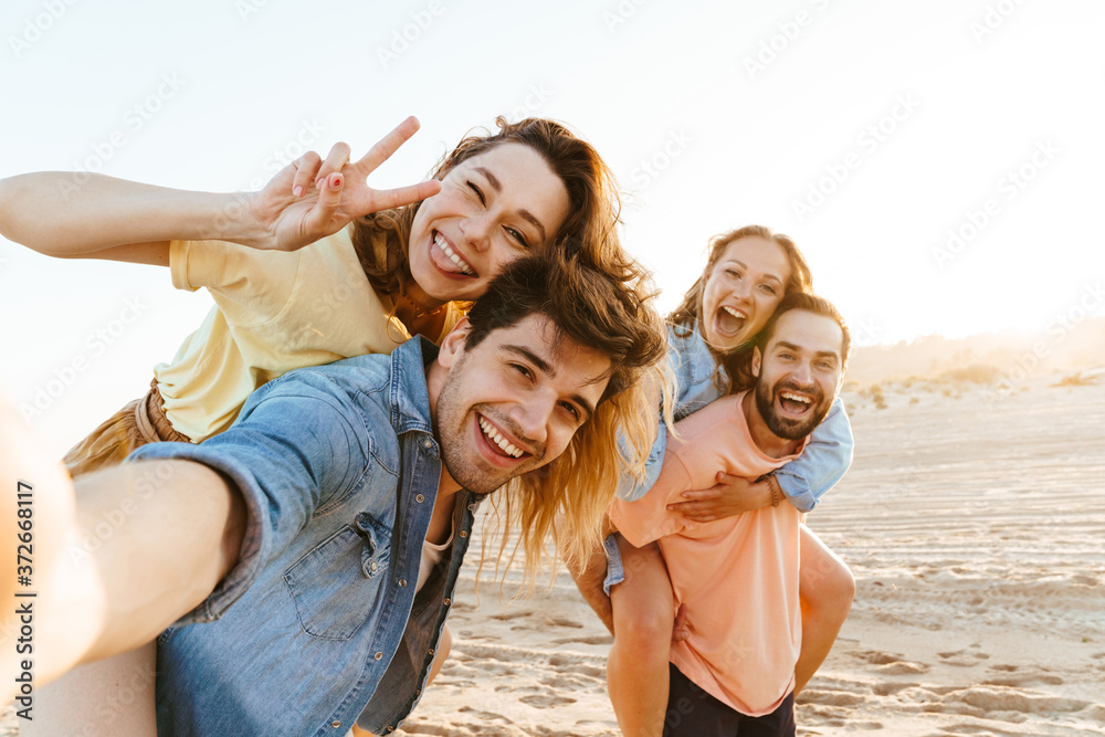 Image of young people smiling and taking selfie while walking on beach Image of young people smiling and taking selfie while walking on beach