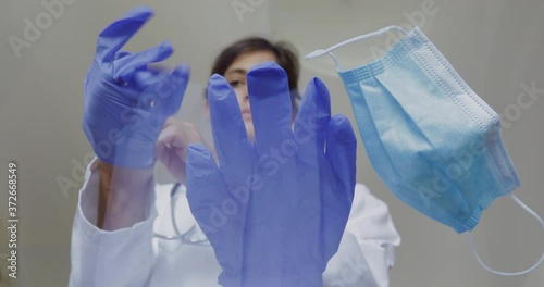 Female doctor or nurse is preparing to receive patients during an epidemic. She puts on a medical mask and disposable gloves. 