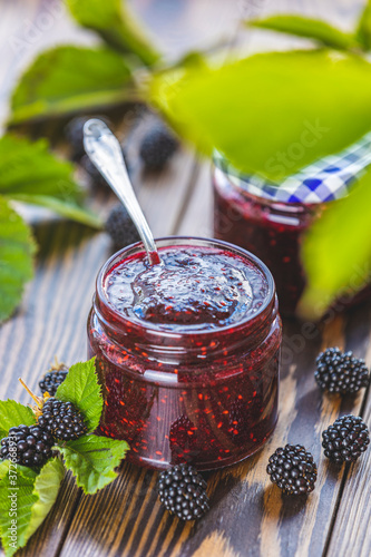 Fresh homemade blackberry jam in glass jar on a wooden background. Several fresh berries are near it.
