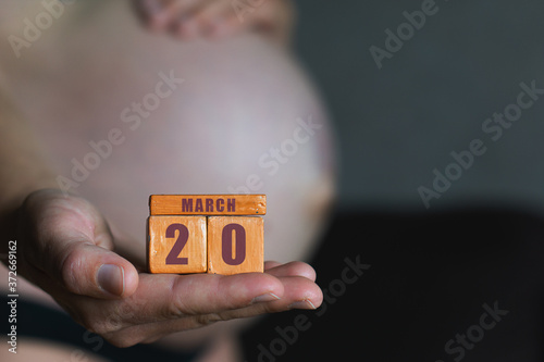 march 20th. Day 20 of month,planned date of birth. Month and day placed on wood calendar in pregnant womans hand. spring month, day of the year concept