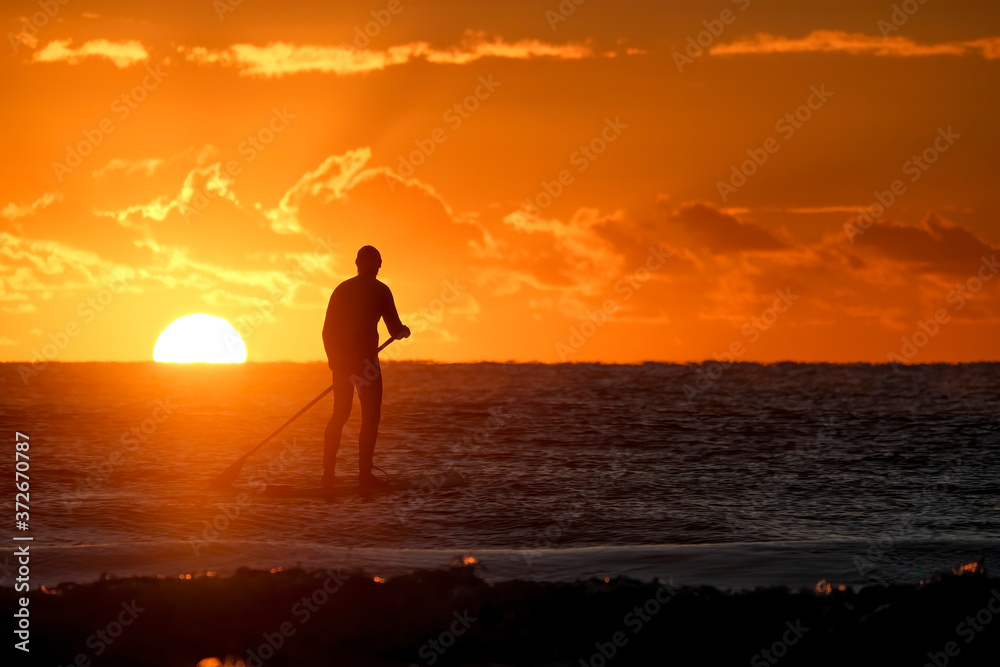 A silhouette of a stand Up Paddle Border on the water as the sun rises on the horizon.
