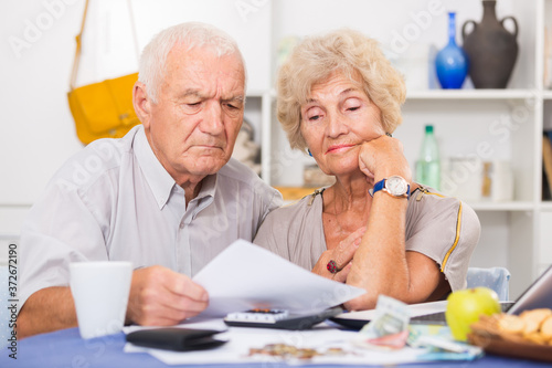 Upset retired couple calculating domestic finances with calculator and bills on table