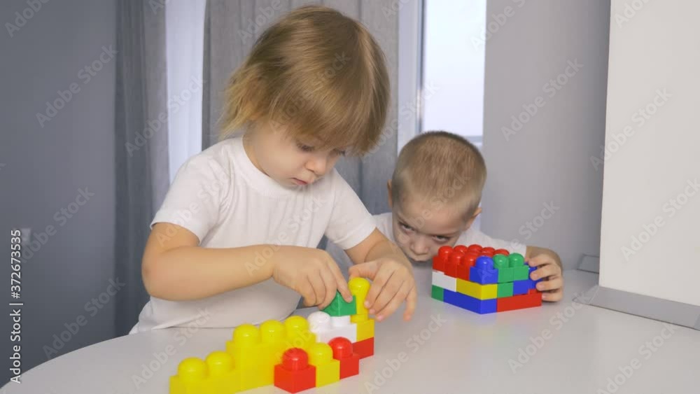 Happy children at home at the table build a house of colored cubes. Preschoolers play with Bricks. Happy children at home at the table build a house of colored cubes. Preschoolers play with Bricks.
