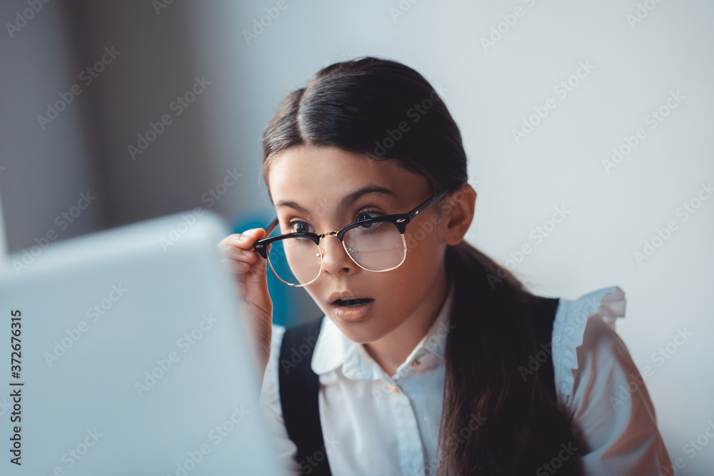 Surprised brunette girl in eyeglasses looking at the laptop Surprised brunette girl in eyeglasses looking at the laptop