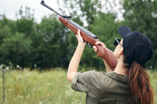 Woman on nature holding a gun up hunting back view black cap 