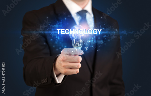 Businessman holding light bulb with TECHNOLOGY inscription, innovative technology concept