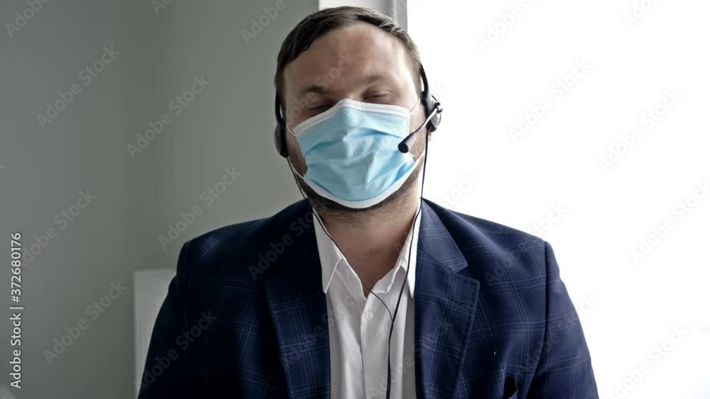 Middle-aged man in a business suit, with headphones and a medical mask. Online communication during the coronavirus epidemic. Middle-aged man in a business suit, with headphones and a medical mask. Online communication during the coronavirus epidemic.