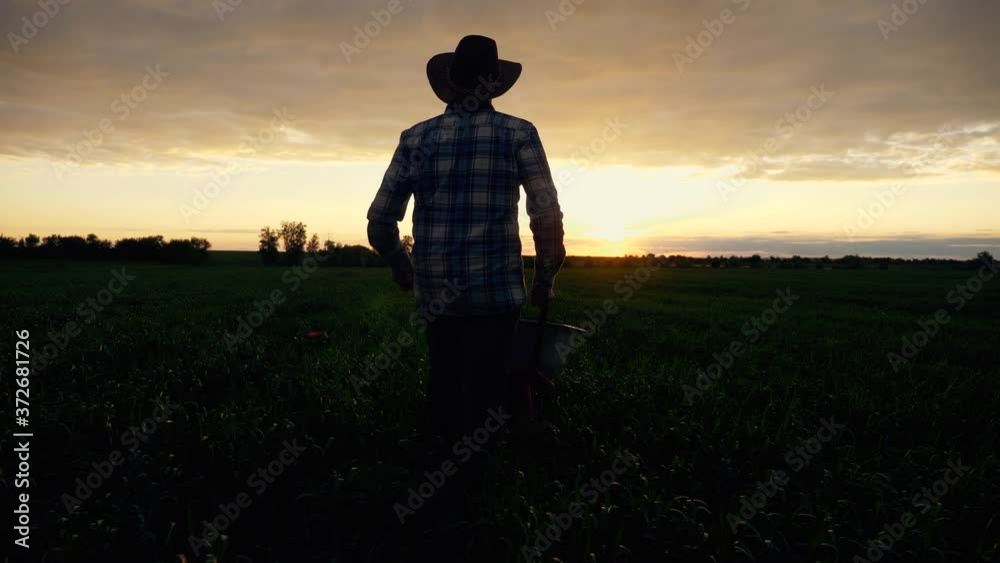 Silhouette of a male farmer at sunset in a meadow pushing a garden wheelbarrow. The lifestyle on the ranch. Peasant labor, Eco-culture. Silhouette of a male farmer at sunset in a meadow pushing a garden wheelbarrow. The lifestyle on the ranch. Peasant labor, Eco-culture.