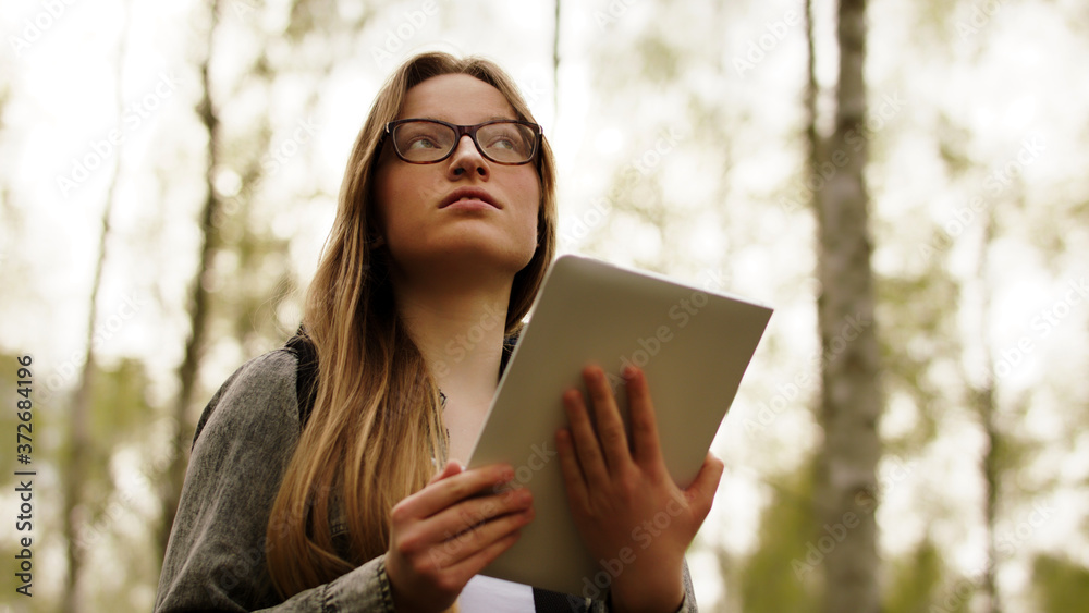 Young caucasian woman tourist with backpack and tablet walking in the forest. low angle. High quality photo Young caucasian woman tourist with backpack and tablet walking in the forest. low angle. High quality photo