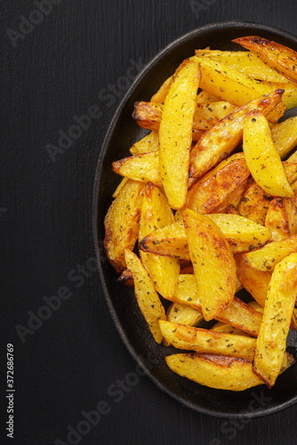 Fried potatoes in a rural style, with spices. On rustic pan, on a wooden black table