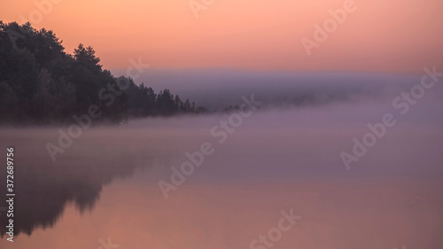 Pink sunrise with thick fog on a forest lake