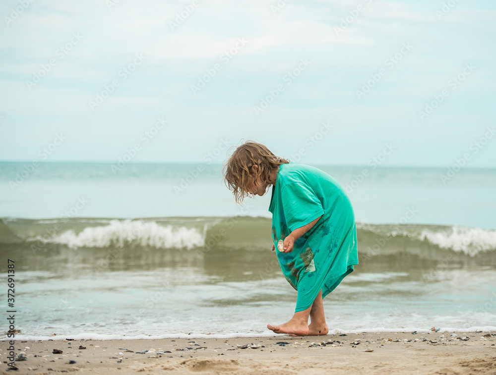 Little kid girl at the sea beach collects seashells. Child steps and waves. Happy childhood. summer vacation at sea or ocean.