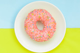 Top view, pink glazed donut on white plate on pastel green turquoise background