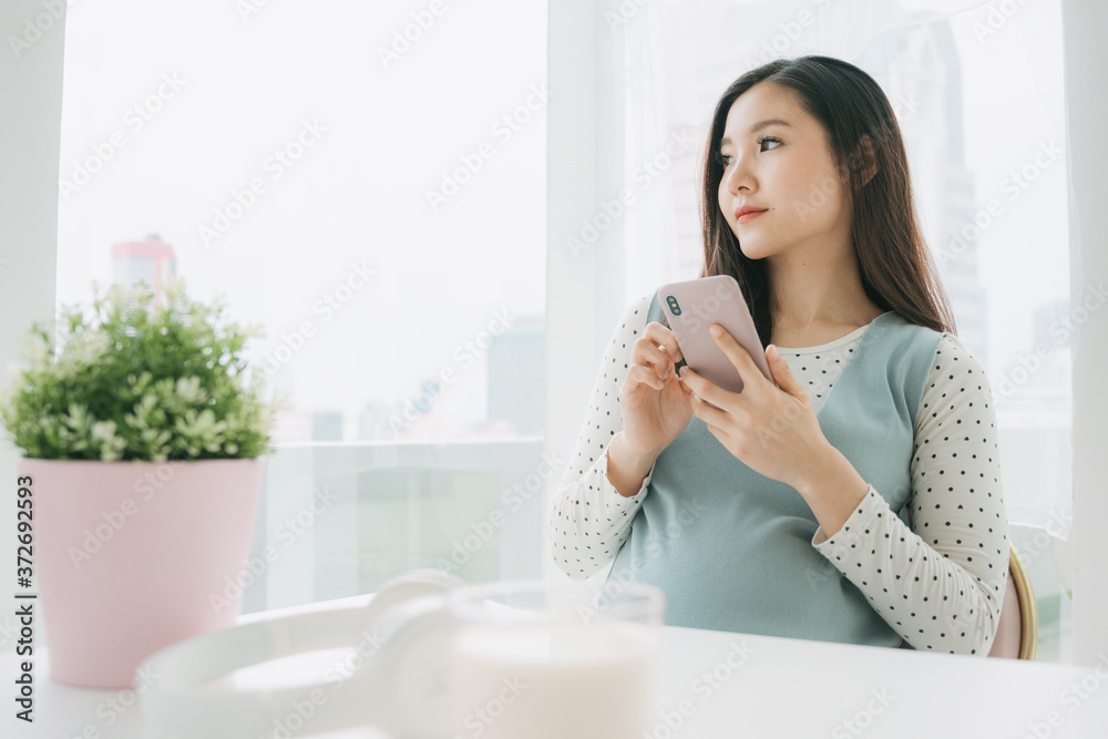 Young beautiful pregnant asian woman using smartphone at home. Young beautiful pregnant asian woman using smartphone at home.