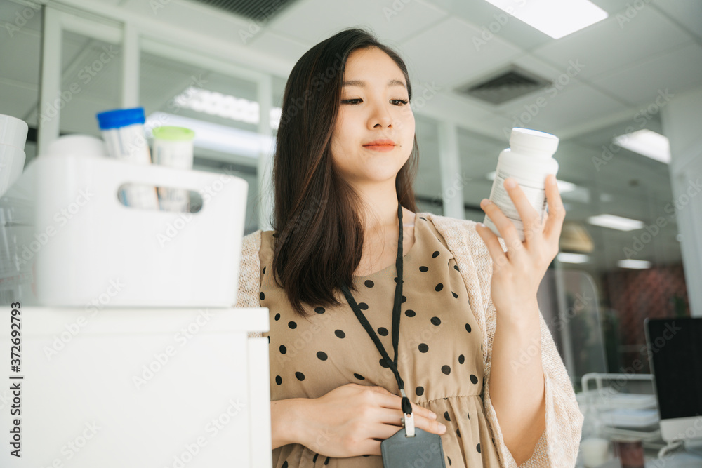 Beautiful pregnant asian businesswoman reading label on medical bottle. Beautiful pregnant asian businesswoman reading label on medical bottle.