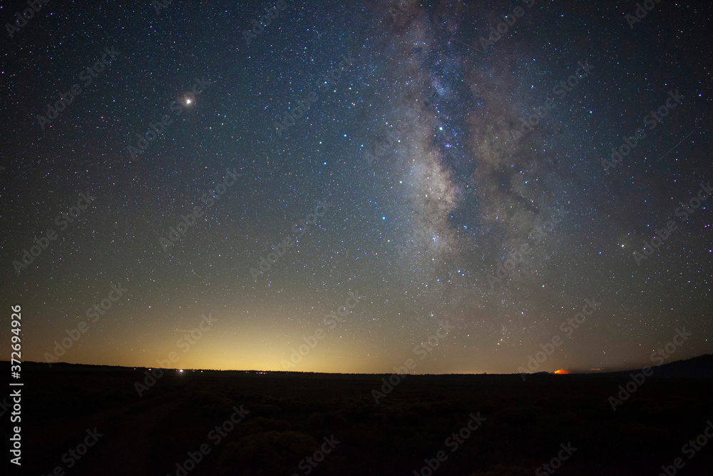 Milky Way stars above a vast prairie with a distant fire 