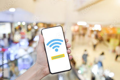 Close-up of hand holding mobile smartphone with wifi connect on blurry shopping mall background.