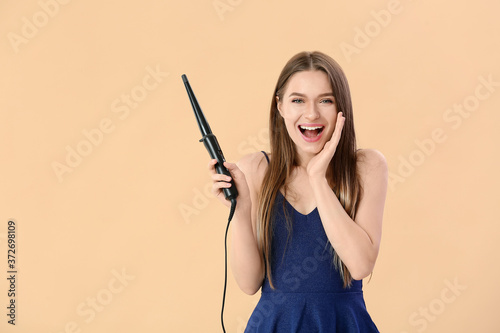 Leinwand Poster Young woman with curling iron on color background