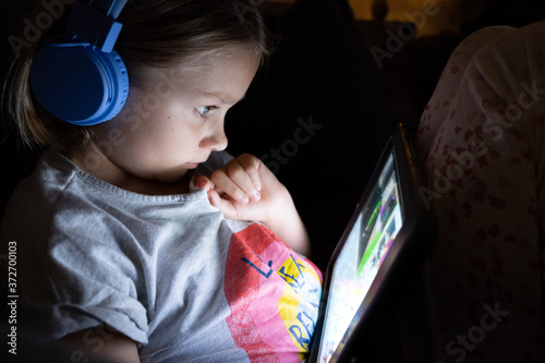 little girl on a tablet with blue head phones in a dark room