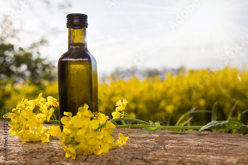 Bottle of rapeseed oil (canola) and rape flowers bunch on table