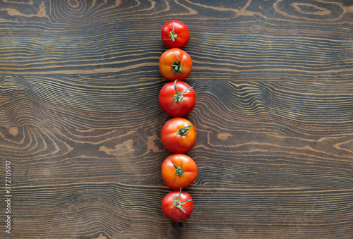 A set of six ripe tomatoes. Vegetables are located hardly one after another on a wooden table. Natural surface. Organic vegetarian food. Harvesting. View from above.