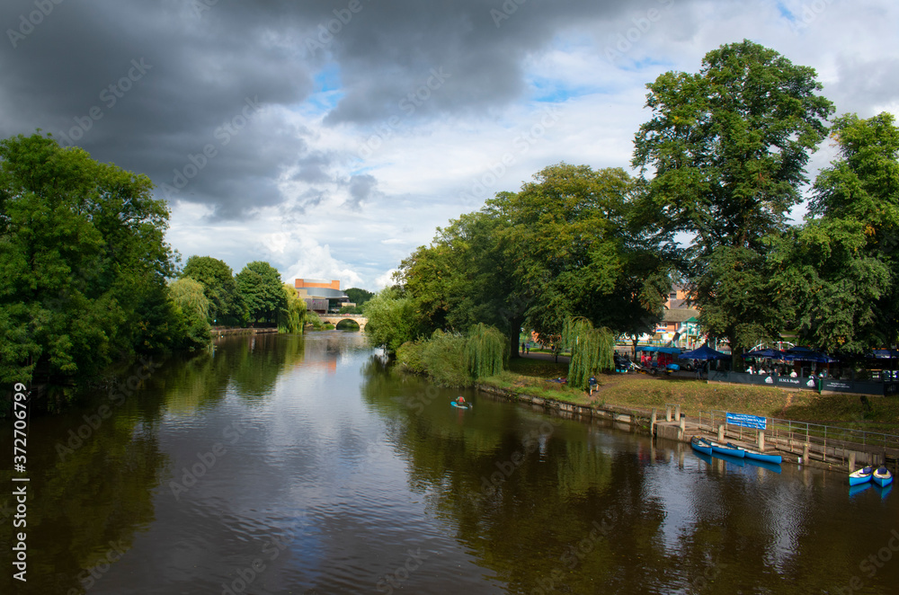The river Severn flowing through the beautiful English town of Shrewsbury. Trees line the river bank and are reflected in the calm river waters. A peaceful summers scene. Copy space.