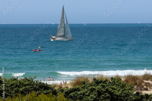 Boat passing in front of the sand dunes that give access to La Barrosa beach in Sancti Petri, Cádiz, Spain.