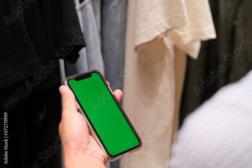 over shoulder of hand holding green screen smart phone in front of many clothing