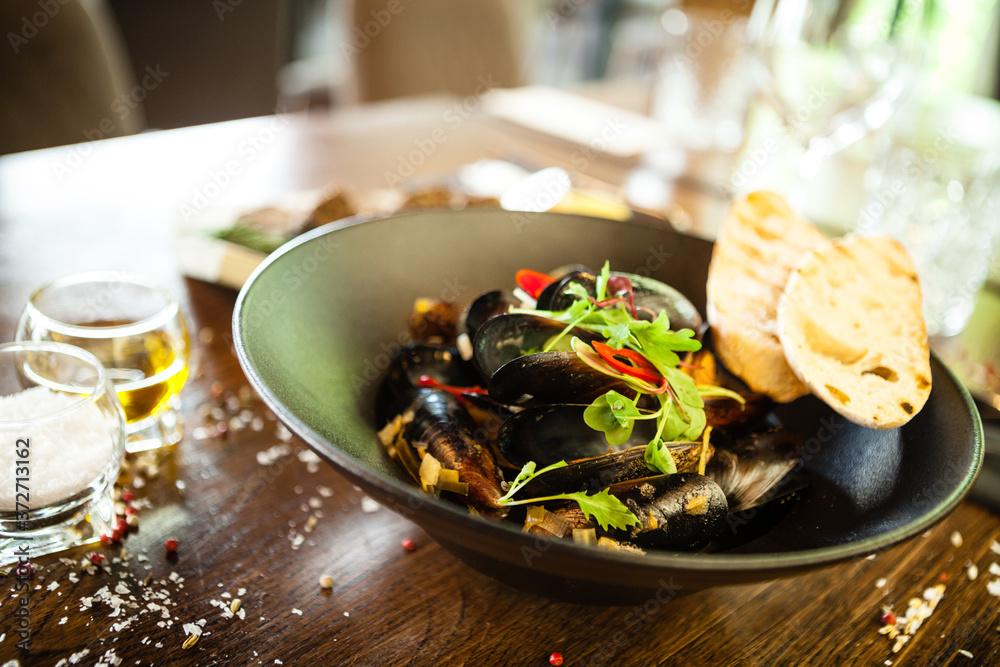 Blue mussels in white wine sauce in black bowl. Delicious healthy seafood closeup served on a table for lunch in modern cuisine gourmet restaurant Blue mussels in white wine sauce in black bowl. Delicious healthy seafood closeup served on a table for lunch in modern cuisine gourmet restaurant