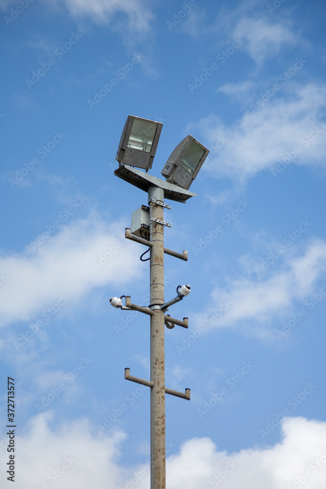 Floodlights above a football pitch with blue sky and clouds in the background Floodlights above a football pitch with blue sky and clouds in the background