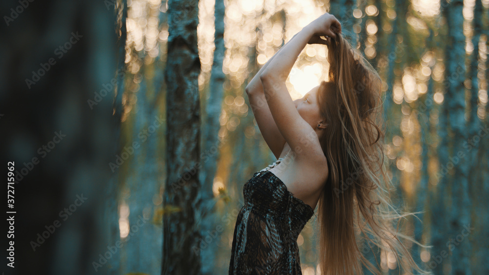 Obraz premium Side view of young caucasian girl playing with her long hair in the forest. . High quality photo