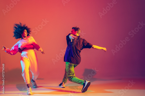 Fototapeta Naklejka Na Ścianę i Meble -  Summer. Stylish man and woman dancing hip-hop in bright clothes on green background at dance hall in neon light. Youth culture, movement, style and fashion, action. Fashionable portrait.