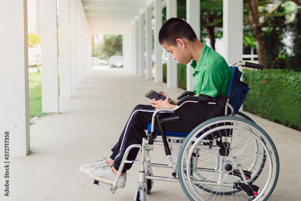 Asian special child on wheelchair is very concentrated with using a smartphone, The ramp for disabled people background, Life in the education age of disabled children, Happy disability kid concept. Asian special child on wheelchair is very concentrated with using a smartphone, The ramp for disabled people background, Life in the education age of disabled children, Happy disability kid concept.