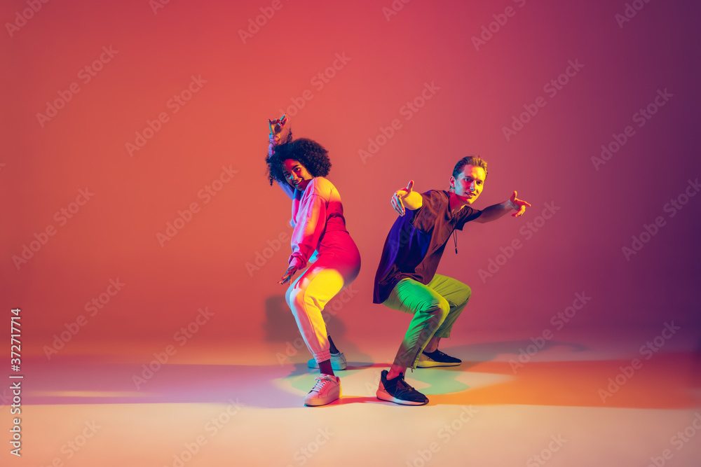 Obraz premium Summer. Stylish man and woman dancing hip-hop in bright clothes on green background at dance hall in neon light. Youth culture, movement, style and fashion, action. Fashionable portrait.