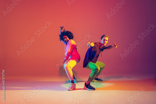 Summer. Stylish man and woman dancing hip-hop in bright clothes on green background at dance hall in neon light. Youth culture, movement, style and fashion, action. Fashionable portrait.
