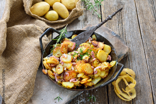 Deftige Bratkartoffeln mit Speck und Zwiebeln rustikal in der Eisenpfanne serviert – Hearty fried potatoes with onions and bacon served in an iron pan