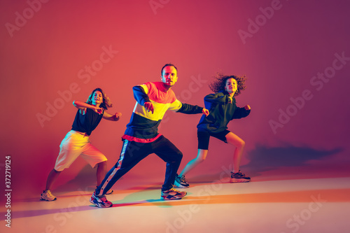 Won't stop the music. Stylish men and woman dancing hip-hop in bright clothes on green background at dance hall in neon light. Youth culture, movement, style and fashion, action. Fashionable portrait.