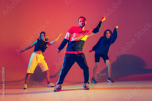 Won't stop the music. Stylish men and woman dancing hip-hop in bright clothes on green background at dance hall in neon light. Youth culture, movement, style and fashion, action. Fashionable portrait.