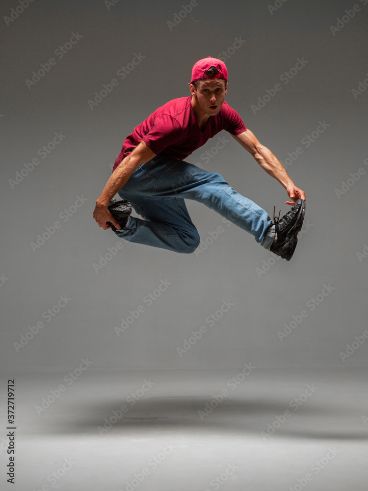 Cool young guy breakdancer jumps in studio on gray background. Battle competitions announcement