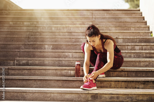 Woman athlete tying the laces on sneakers while sitting on the sills